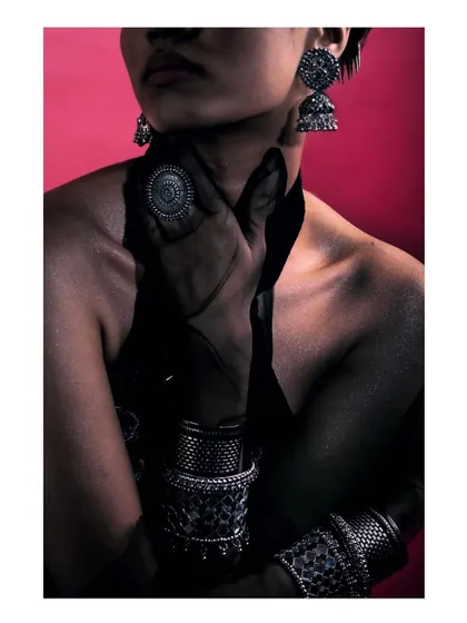 A dark and moody close-up from 'Silver Jewels of Bombay,' where the model's hand, adorned with rings and bracelets, rests on her neck. The image uses shadow to create a sense of intimacy and mystery.