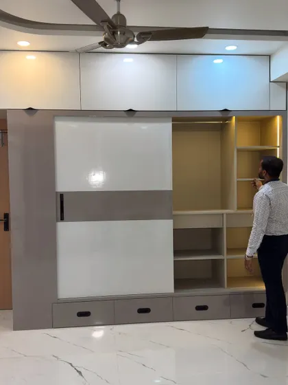 A full view of a large sliding wardrobe with a two-tone glossy finish. The design includes external drawers at the bottom for easy access and lofts on top for seasonal storage, covering the entire wall for a built-in look.