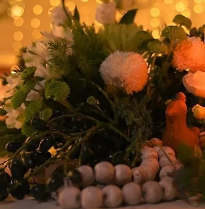 A table centerpiece featuring a mix of white flowers, greenery, and unique textural elements, all illuminated by the soft glow of a pillar candle.