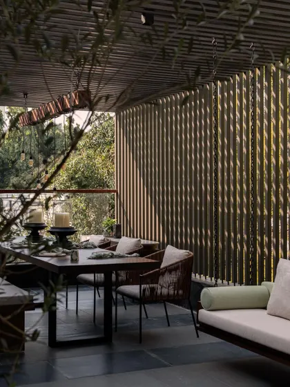 The terrace dining area at Pràna, shaded by a wooden pergola. The dappled sunlight filtering through creates a beautiful, calming atmosphere for outdoor meals.