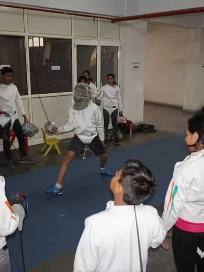 A coach demonstrates a technique to a group of young fencers during a training session. Observational learning is key before students practice the moves themselves.