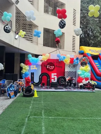 An epic Hot Wheels party setup in an outdoor space, complete with a large inflatable slide, a racetrack stage, and themed character cutouts.