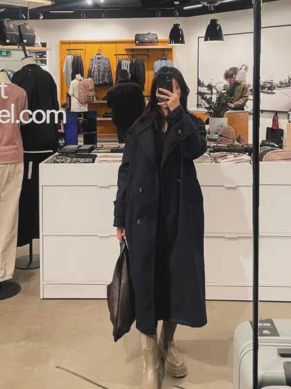 A store mirror selfie showing off a long navy trench coat, a perfect piece for fall.
