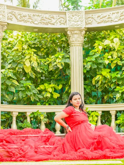 A beautiful portrait of a mom-to-be sitting in a garden gazebo. The red gown spreads out on the grass, creating a stunning visual.
