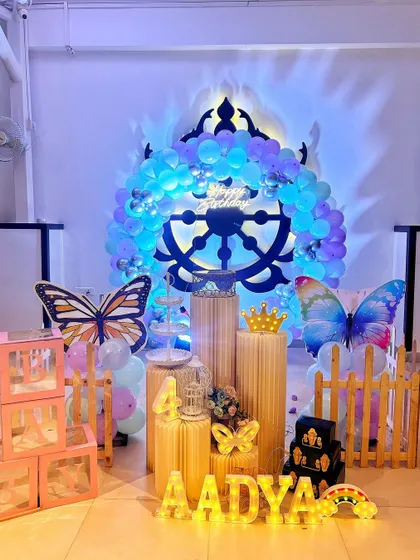 A magical butterfly themed fourth birthday setup, featuring a large decorative backdrop, butterfly props, and the child's name in lit-up letters.