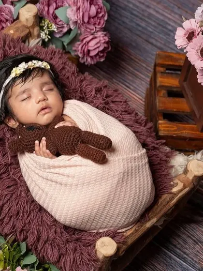 This is a wider view of a floral-themed setup, showing how I use props like a miniature wooden bed and crates of flowers to build a beautiful scene. The baby is kept safe and comfortable while I create this artful portrait.