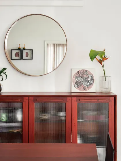 A mahogany wood credenza with fluted glass doors in our 'Rustic Minimal' project. This piece provides stylish storage while the round mirror above it enhances the sense of space and light in the dining area.
