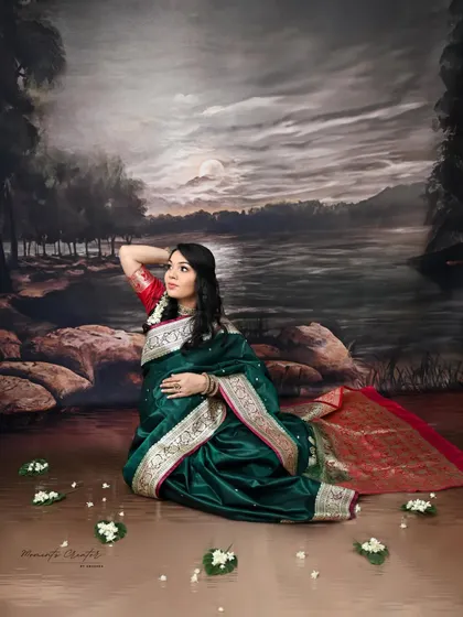 A painterly and artistic portrait. The mom-to-be, dressed in a traditional green saree, is posed against a scenic, moonlit backdrop, creating a timeless and poetic image.