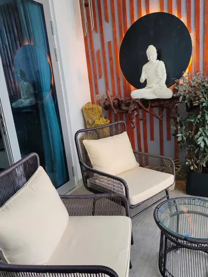 A serene and stylish balcony seating area. A white Buddha statue sits against a dramatic backdrop of wooden strips and a black circular panel, creating a tranquil and meditative corner.