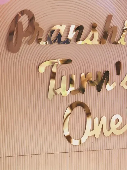 A close-up of the elegant gold mirror text for "Pranshi Turn's One," which adds a reflective, high-end finish to the main backdrop.