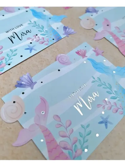 We also create personalized stationery for little ones, like these mermaid-themed 'With Love' cards. The design features die-cut mermaid tails and seashells with silver foil accents, making them a thoughtful gift.