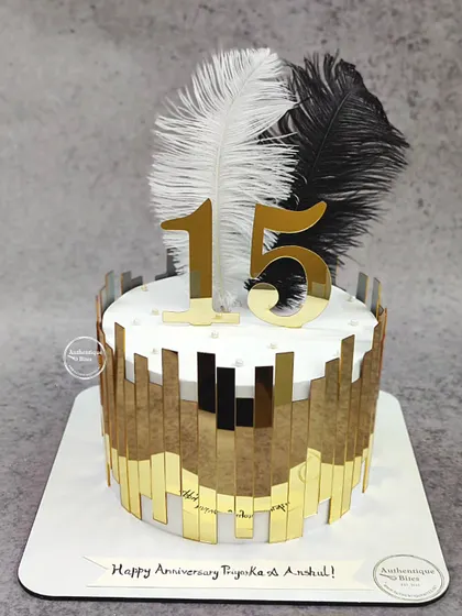 A grand 15th-anniversary cake with a modern design. This cake features dramatic black and white feathers and a reflective gold panel design, creating a bold and artistic statement.