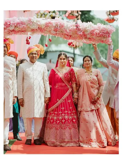 The emotional moment of the bride walking down the aisle with her parents under a beautiful floral canopy.