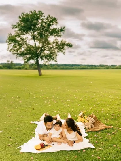 A family lies together on a picnic blanket in a vast green field under a dramatic sky. This wide-angle shot captures a sense of peace and connection, emphasizing the family in a beautiful landscape.