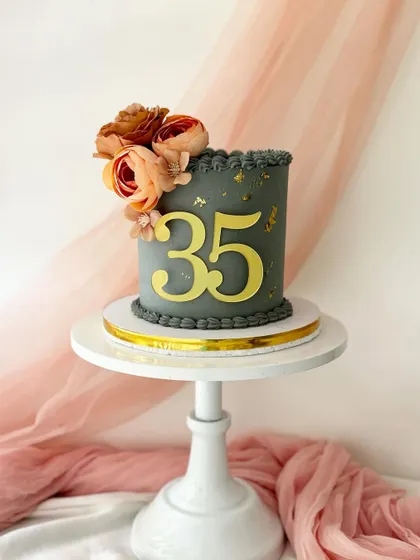 A chic grey cake for a 35th birthday. The minimalist design is enhanced with a large gold number topper and a simple arrangement of silk flowers.