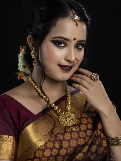 This classic pose highlights the rich colors of the makeup. The deep lip color and warm eyeshadow tones are chosen to perfectly complement the bride's maroon silk saree and gold jewellery.