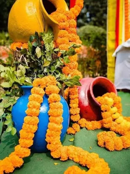 A decorative arrangement of colorful pots with marigold garlands spilling out, used as props for pre-wedding functions.
