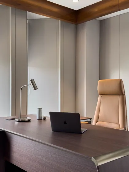 A close-up of the executive desk and ergonomic chair. The clean lines of the desk, minimalist lamp, and high-back leather chair reflect a focus on uncluttered, high-performance workspace design.