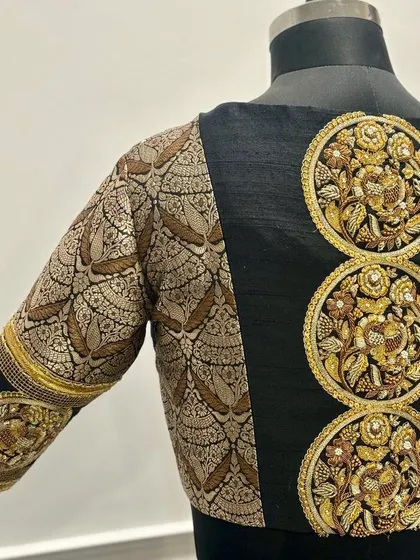 A striking black blouse featuring a combination of brocade fabric and hand-embroidery. The back is adorned with three large circular motifs, intricately embroidered with gold thread in traditional patterns, creating a bold and artistic statement.
