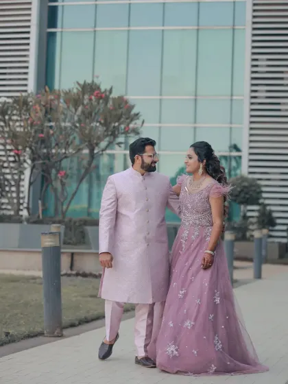 A full-length shot of the couple walking in their stunning engagement attire. The modern architectural background provides a clean and sophisticated setting for this elegant portrait.