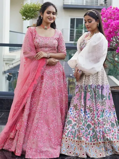 Here you can see two of my distinct lehenga styles side-by-side. On the left, a classic pink embroidered lehenga, and on the right, a modern raw silk piece with multicolor floral embroidery and puffed sleeves.