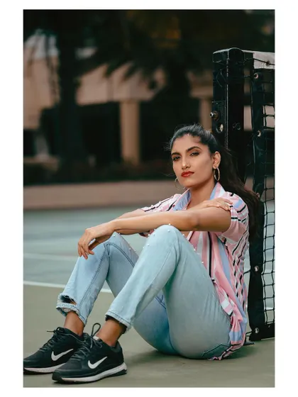 A casual outdoor portrait on a tennis court. The setting adds a sporty, lifestyle element to this fashion-forward shot.