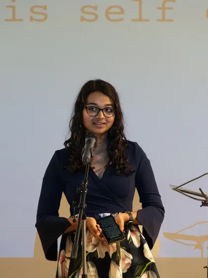 A young writer confidently performing her piece at the 'Verse & Voice' showcase. We create opportunities for emerging poets to gain valuable stage experience.