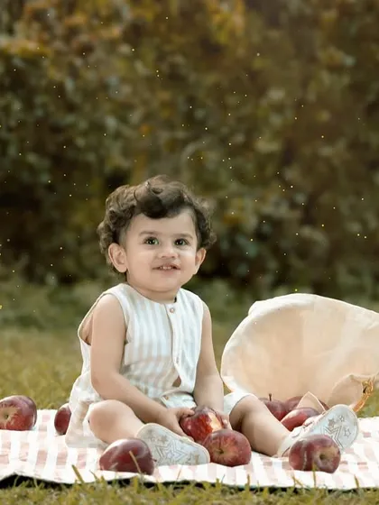 A one-year-old boy sits on a picnic blanket in a park, surrounded by apples. This outdoor milestone shoot uses natural elements to create a fresh and timeless birthday portrait.