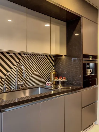 A bold and artistic kitchen design featuring a geometric-patterned backsplash. The matte grey cabinets and integrated coffee machine create a highly modern and sophisticated look.