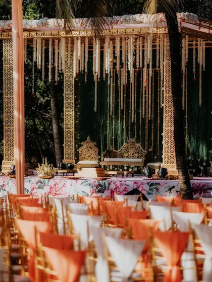 An ornate golden mandap designed for a traditional wedding. The intricate laser-cut panels and hanging floral strings create a rich, luxurious atmosphere for the main ceremony.