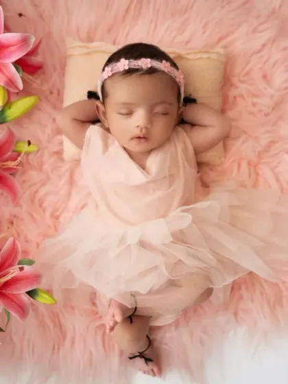 A beautiful overhead shot of a newborn girl in a pink dress, lying on a soft rug and framed by pink lilies and peonies. This setup creates a dreamy, fairytale-like portrait.