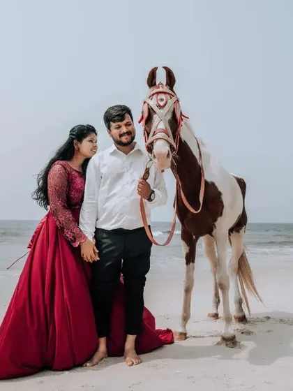 A full-length shot of a couple on the beach with a horse, showcasing the entire scene and the bride's beautiful red gown.
