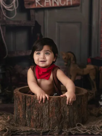 This little cowboy is peeking out of a rustic barrel in our Old West themed studio setup. We love creating playful scenarios that bring out a child's personality.