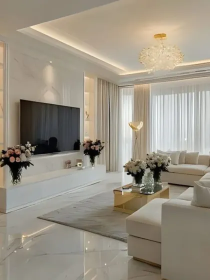 We designed this bright, glamorous living room with all-white furniture, polished marble floors, and gold accents. The space is filled with bouquets of white flowers, enhancing the fresh and luxurious feel.