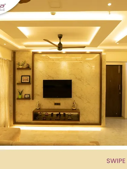 This living room features a grand TV unit with a marble-finish back panel framed by wood. The false ceiling with cove lighting adds to the sense of height and luxury.