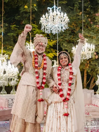 A moment of pure joy as the couple celebrates their union after the varmala, with hands raised in triumph under the sparkling chandeliers.