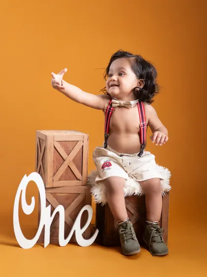 A candid moment from a first birthday photoshoot. The baby reaches out with a joyful expression, perfectly capturing the excitement of this milestone against a warm, rustic set.