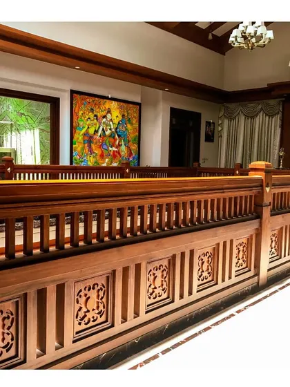 This view showcases the upper level of a residence, with intricately carved wooden railings overlooking the floor below. The inclusion of traditional Indian artwork adds a layer of cultural richness to the interior design.