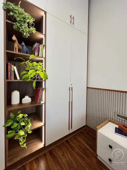 A close-up of a custom wardrobe with integrated open shelving. The shelves are lit with LED strips, creating a beautiful display for books and decor, while adding a touch of biophilic design with trailing plants.