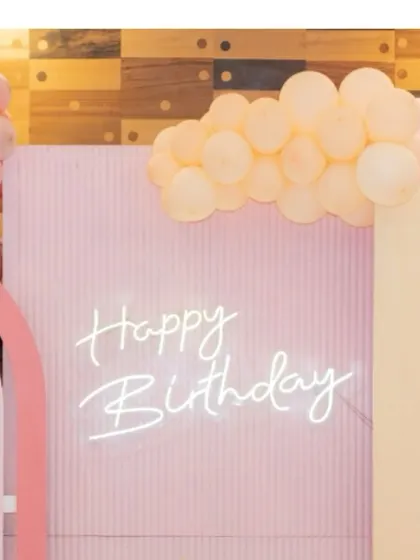 A 'Happy Birthday' neon sign set against a pastel pink backdrop, a simple yet beautiful element for any party theme.