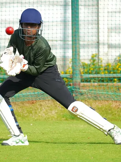 A wicket-keeper in action, eyes locked on the ball as it comes into the gloves. This is focus personified.