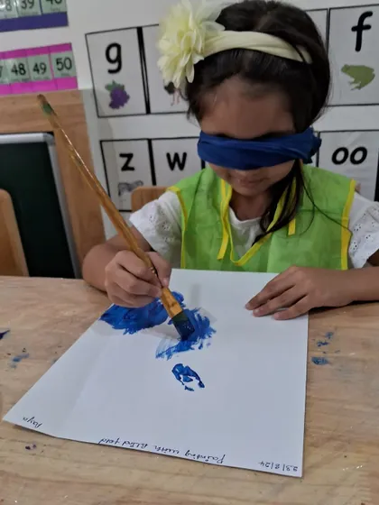 With her eyes covered, this girl uses a paintbrush to make bold blue strokes. It's an exercise in letting go of control and embracing the unexpected results.