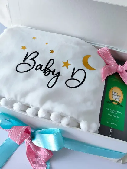 A close-up of a personalized baby blanket and pillow set from the 'Touch of Heaven' hamper. The soft fabric and custom "Baby D" lettering make it a cozy and cherished keepsake.