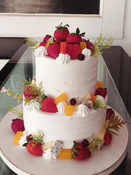 A two-tiered fresh fruit cake, elegantly decorated with strawberries and other seasonal fruits.