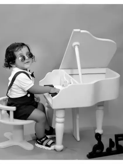 A stylish black and white portrait of a little boy at a miniature piano, giving the photo a classic, old-hollywood feel.