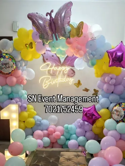 A beautiful pastel butterfly theme for a first birthday. The decoration includes a balloon arch with a large butterfly foil balloon, a light-up number '1', and a neon sign.