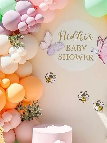 A detailed view of the personalized "Nidhi's Baby Shower" sign, surrounded by pastel balloons and whimsical bee and butterfly accents.
