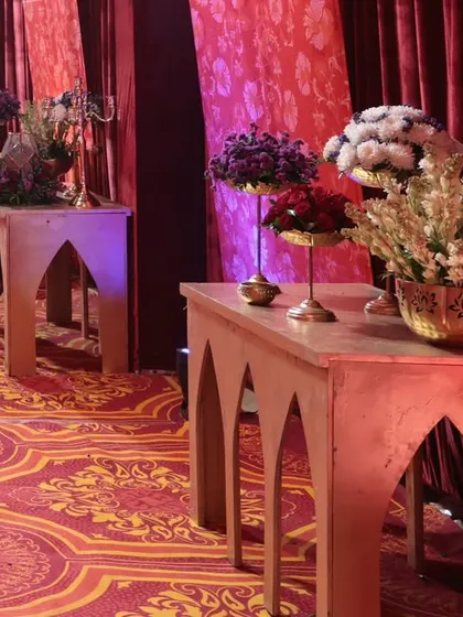 The walkway decor featured a line of console tables with alternating floral arrangements, illuminated by soft purple uplighting against the rich red drapes.