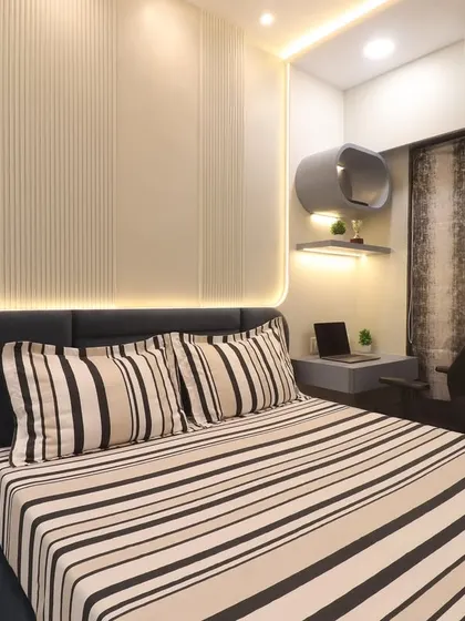 A full view of the Bhayandar West master bedroom, showing the integrated study nook next to the bed. The design uses fluted wall panels and cove lighting to create a calm and sophisticated environment.