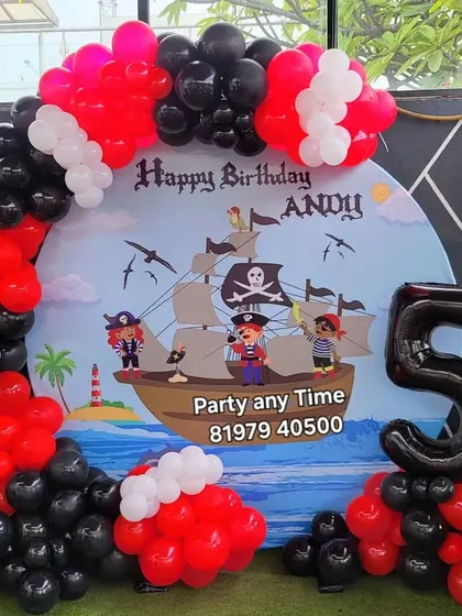 An adventurous pirate theme for a 5th birthday, with a pirate ship backdrop and a red, black, and white balloon arch.